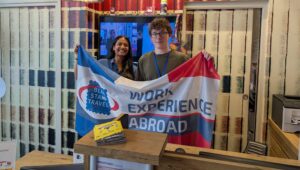 Photo of Work Experience Abroad students at their placement holding a Blue Stamp Travel flag in Lille.