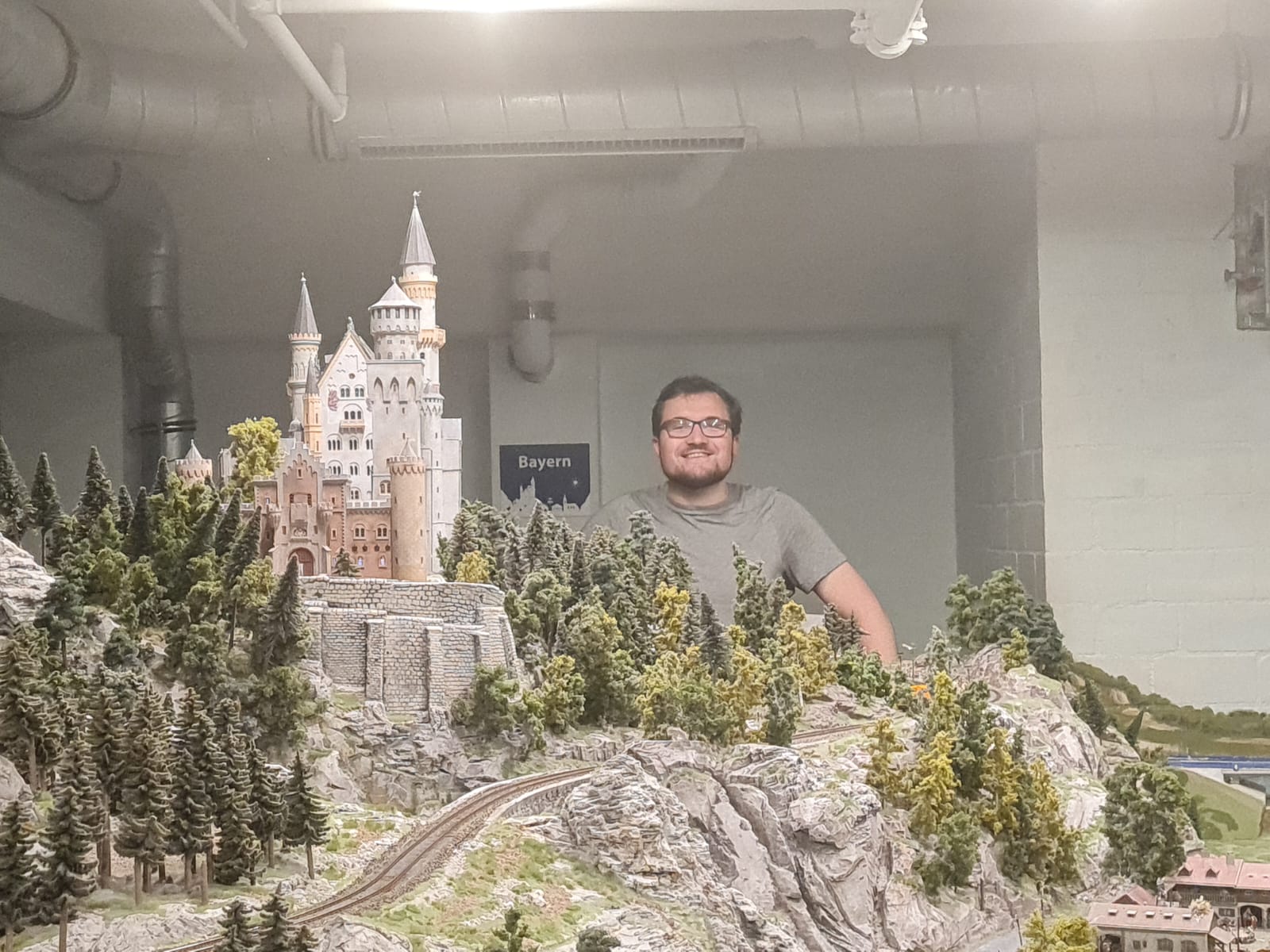 A young man smiles behind a miniature model of Neuschwanstein castle in Miniatur Wunderland