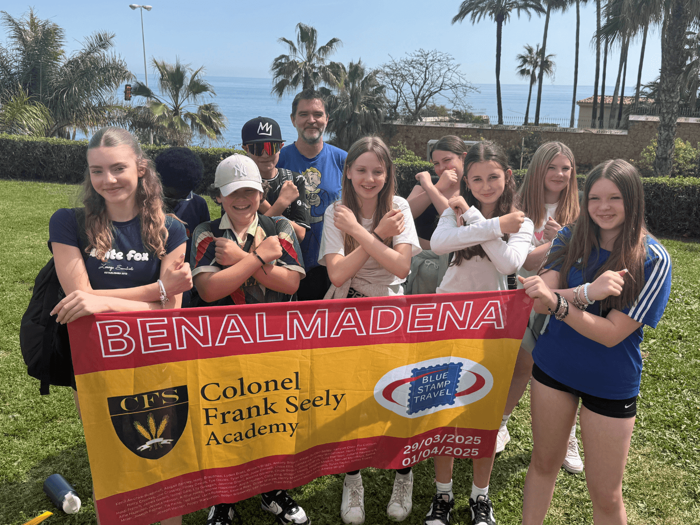 A group of students on a school trip to Andalusia hold up a Blue Stamp Travel banner