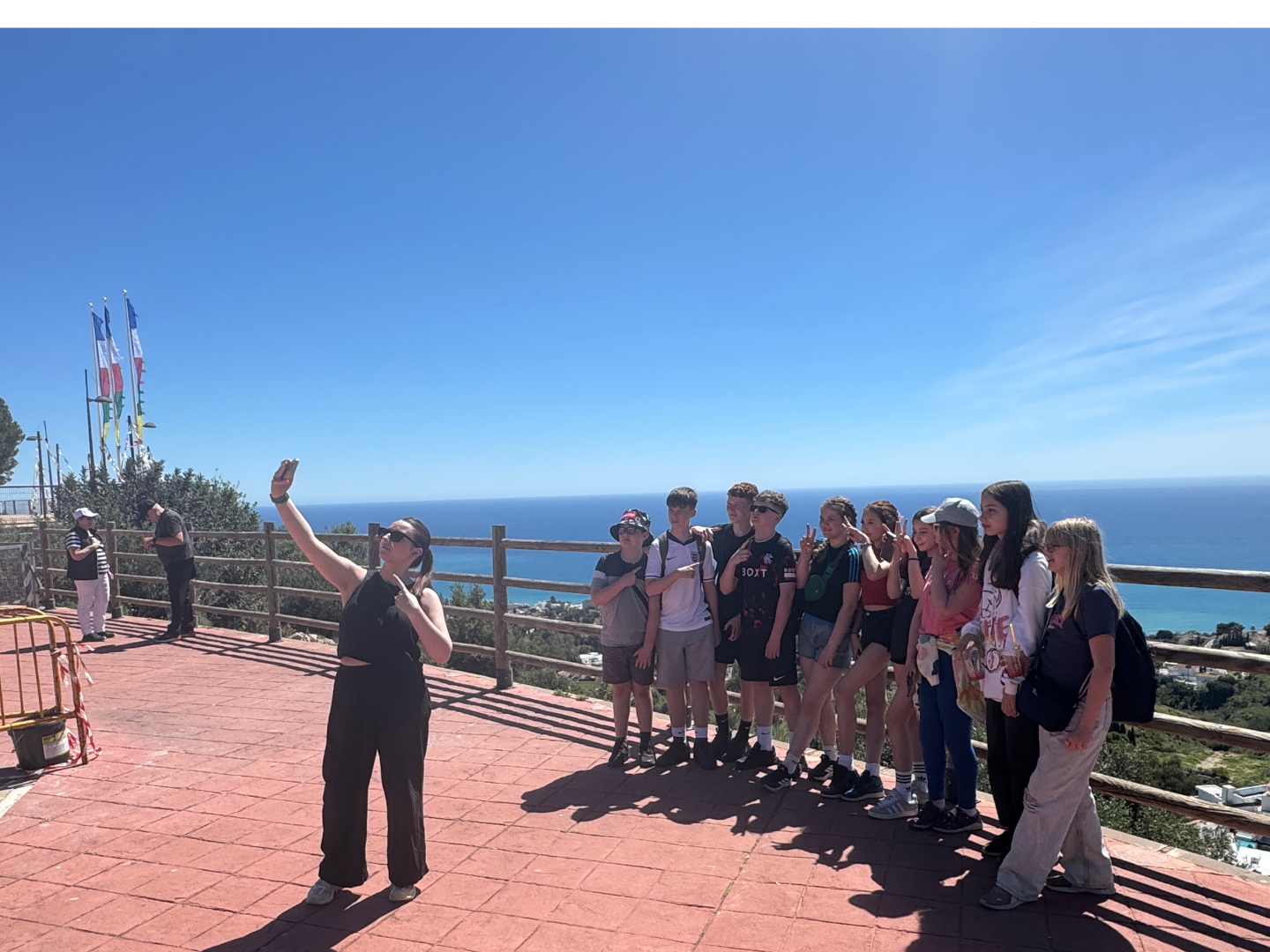 A group of students on a school trip to Andalusia enjoy a group photo on a sunny terrace with the sea in the background