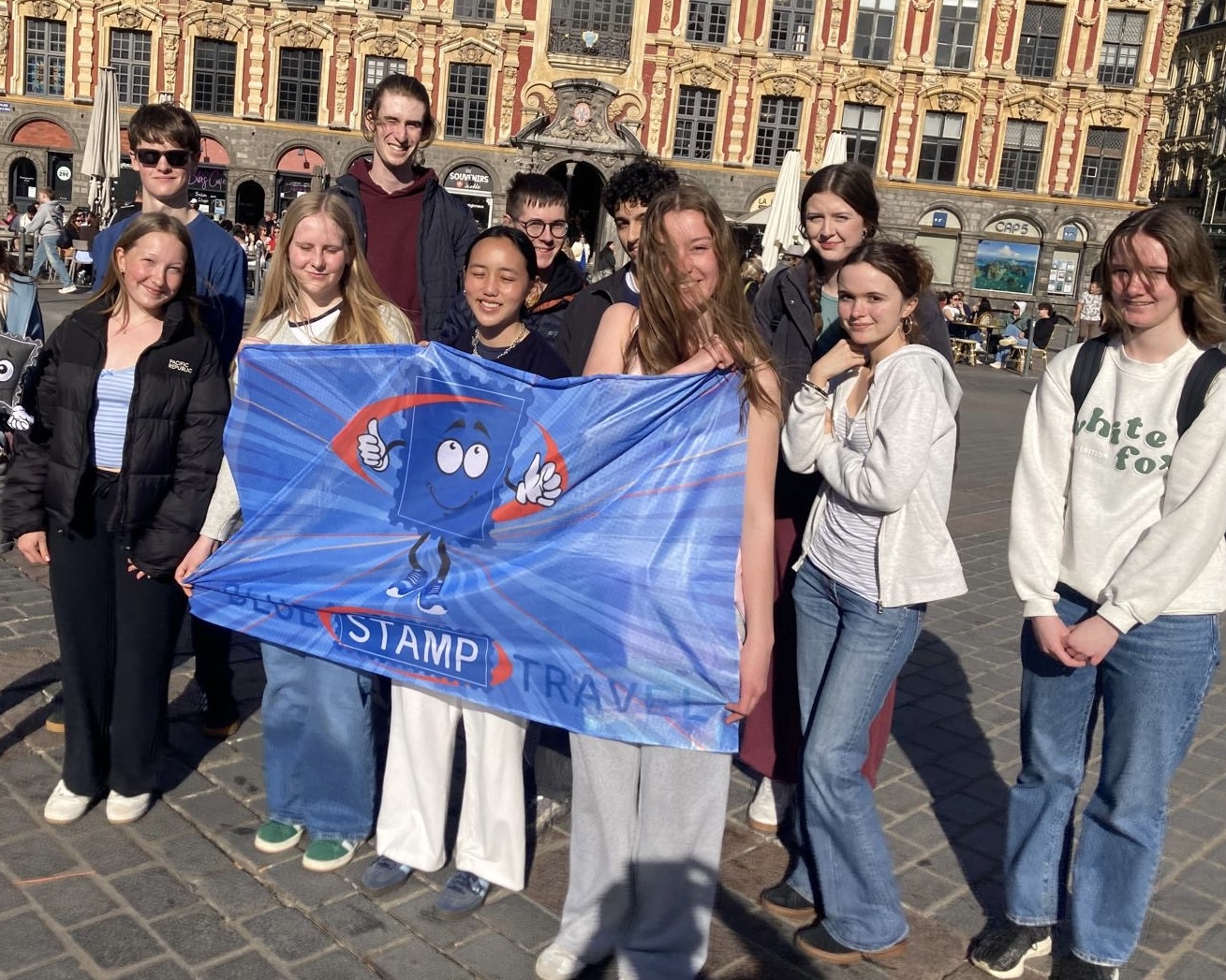 A group of students hold a blue Blue Stamp Travel banner with a grand building in the background