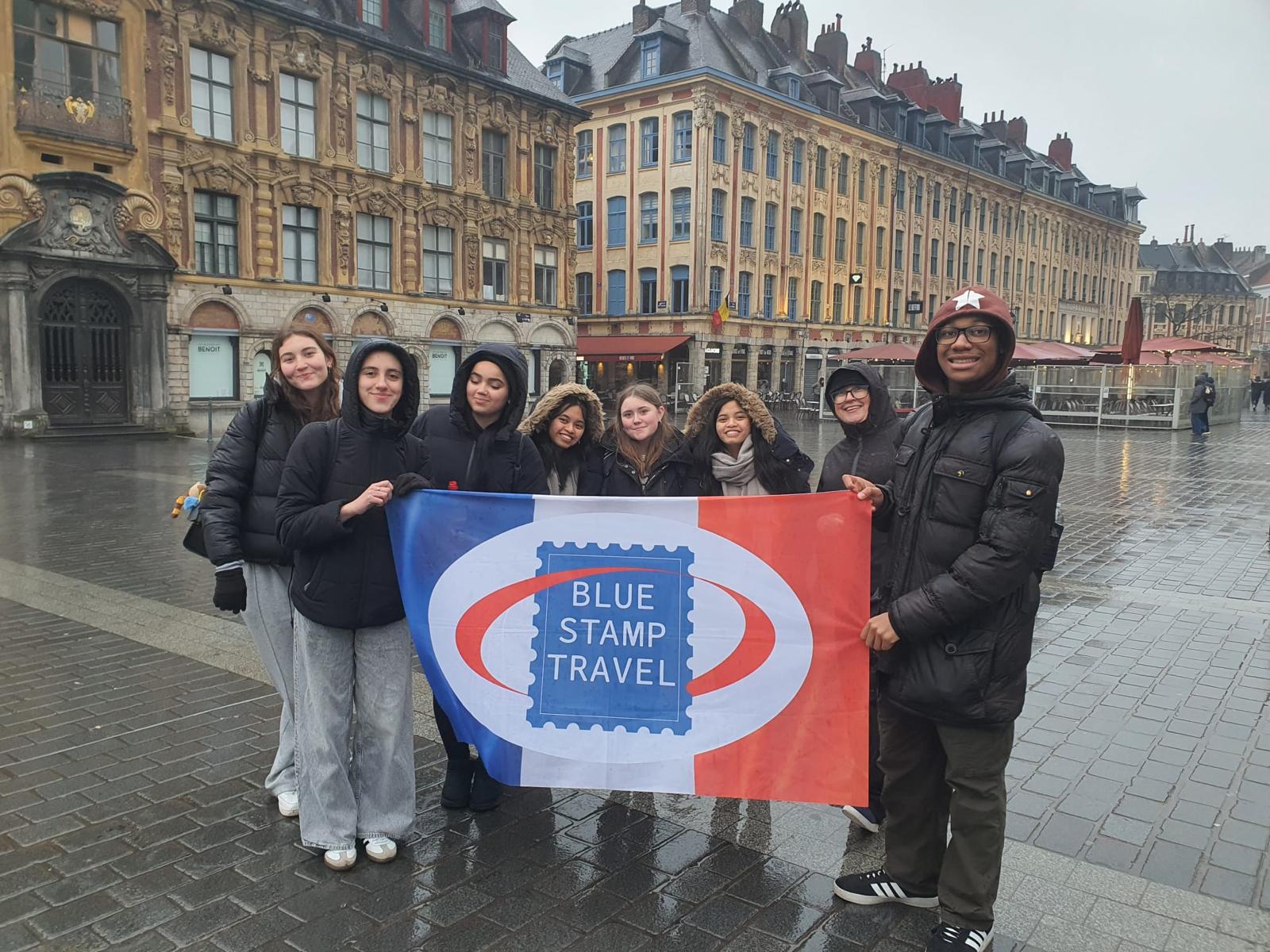 A group of students hold a Blue Stamp Travel banner based on the French flag