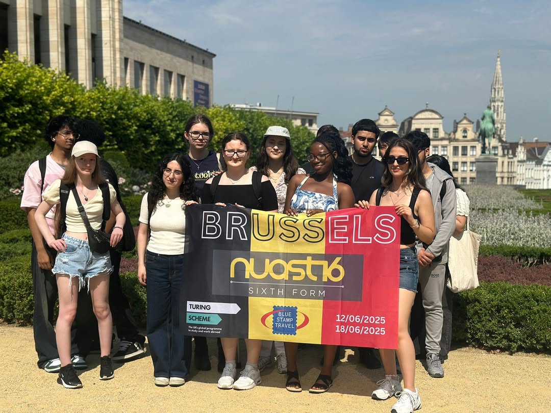 Students on a school trip to Belgium hold up a banner.