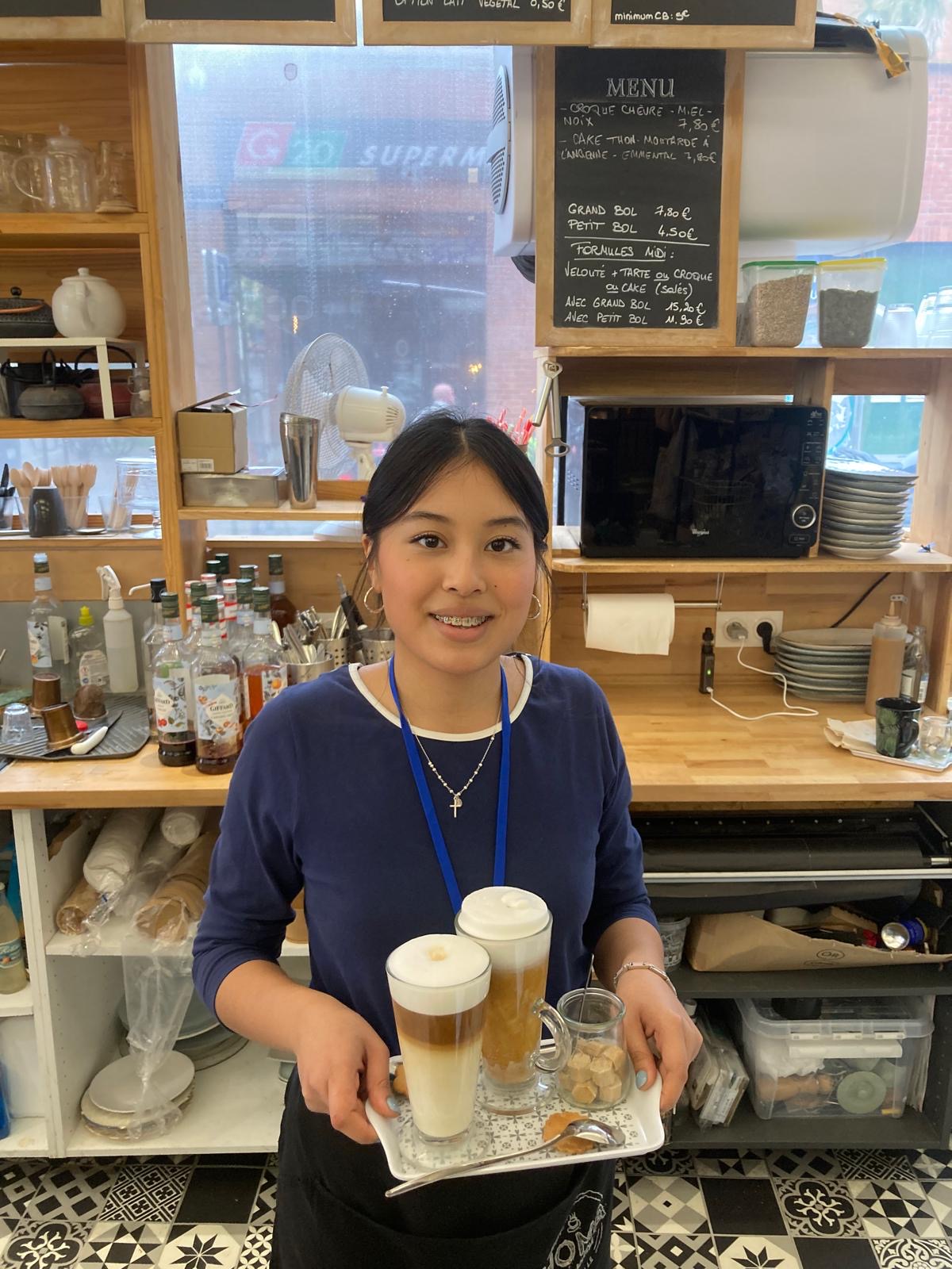 A Work Experience student holds a tray of coffees in a cafe in France