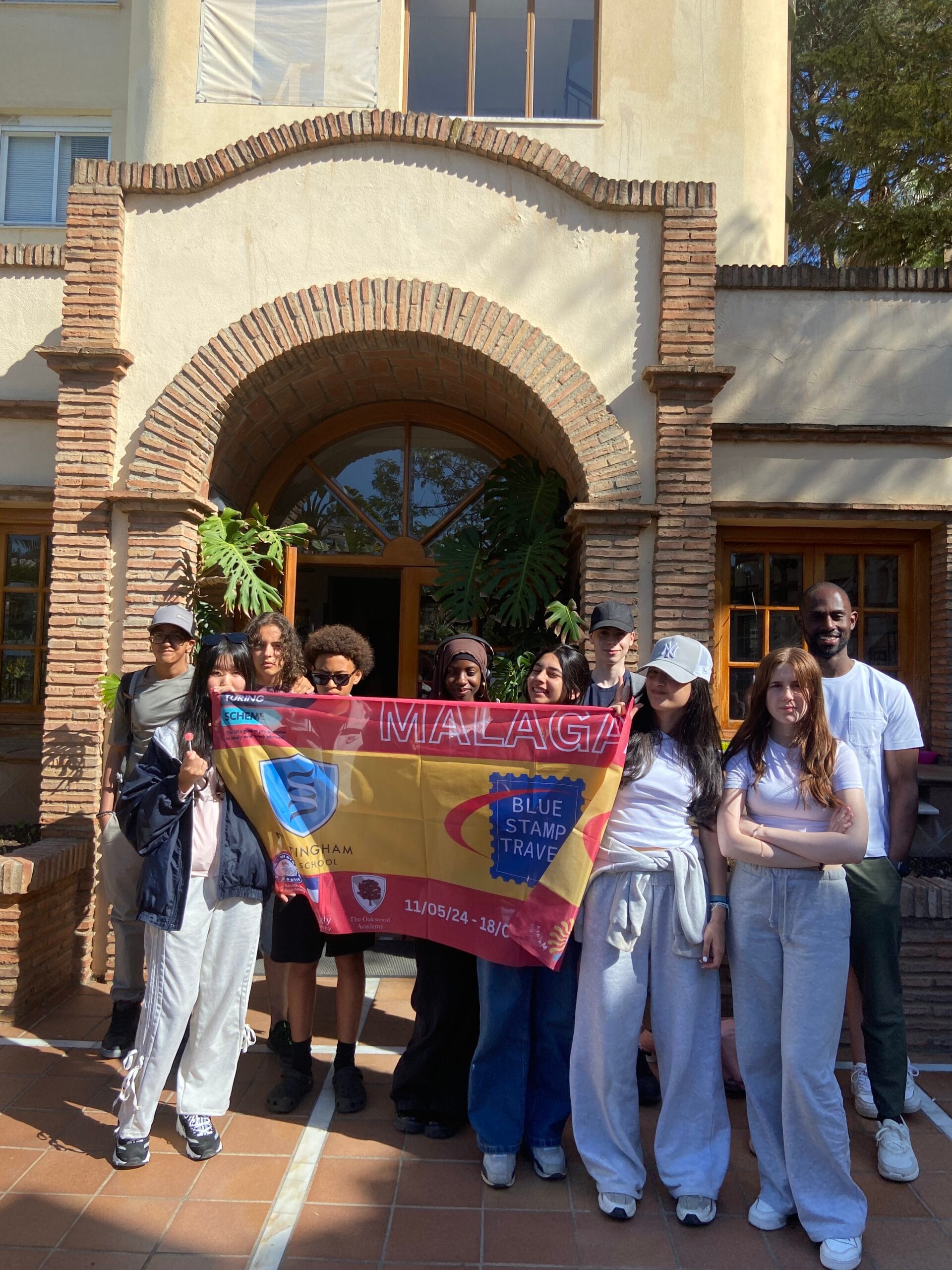 Students and teachers standing outside a language school holding a flag, Nottingham Consortium trip to Malaga, May 2024, organised by tour operator, Blue Stamp Travel.