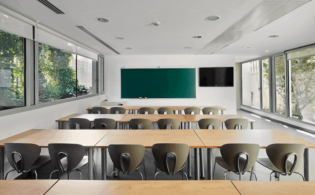 a photo of a classroom tables in a row facing a chalkboard and a monitor screen.