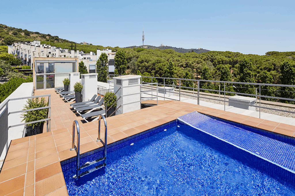 roof-top pool with many sunbeds lined up. There is a lot of greenery in the background.